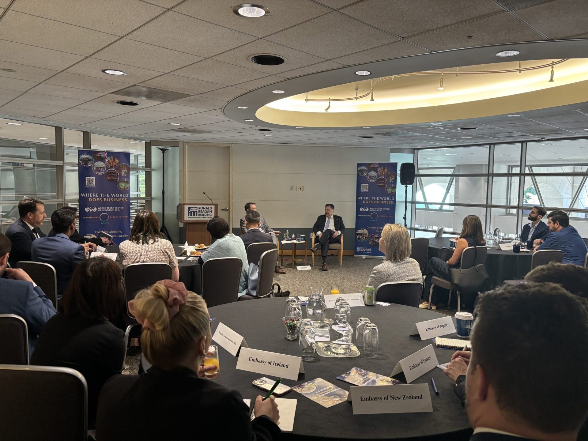 Attendees at round tables with embassy nameplates listening to a speaker during a WITA roundtable discussion at the Ronald Reagan Building